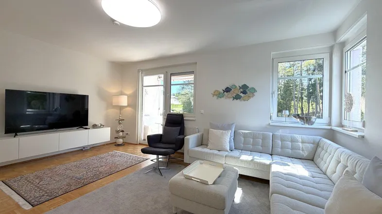 Helles Wohnzimmer mit bequemem Ecksofa, Holzboden und großen Fenstern, die einen schönen Blick ins Grüne bieten.