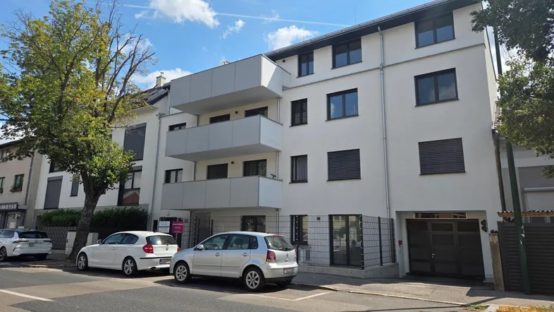 Modernes Mehrfamilienhaus mit weißer Fassade, mehreren Balkonen und Tiefgaragenzufahrt an einer städtischen Straße.