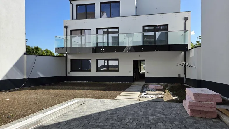 Rückseite eines modernen Neubaus mit Terrassen, Balkonen und einem vorbereiteten Gartenbereich.