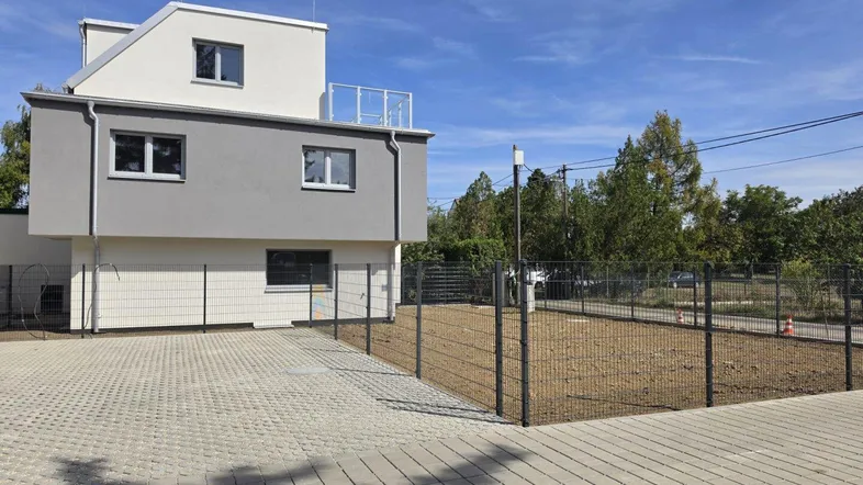 Modernes Gebäude mit grauer Fassade, gepflastertem Parkplatz und eingezäuntem Grundstück.