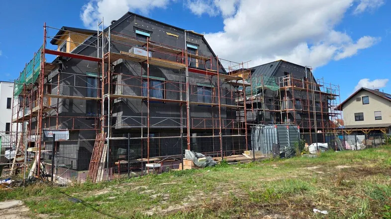 Neubau im Bauzustand mit Gerüst und dunkler Isolierung unter blauem Himmel.