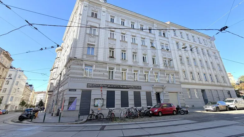 Historisches Eckgebäude in urbaner Umgebung mit Straßenbahnschienen im Vordergrund und klassischer Architektur.