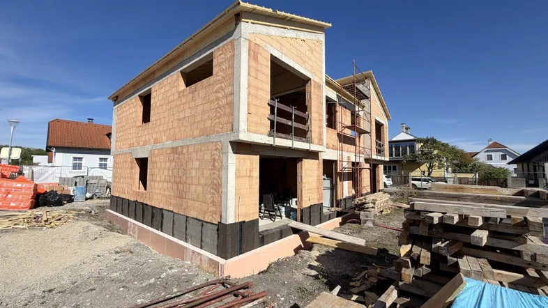Neubau im Rohbauzustand mit sichtbaren Ziegelwänden und Holzkonstruktion des Daches unter blauem Himmel.