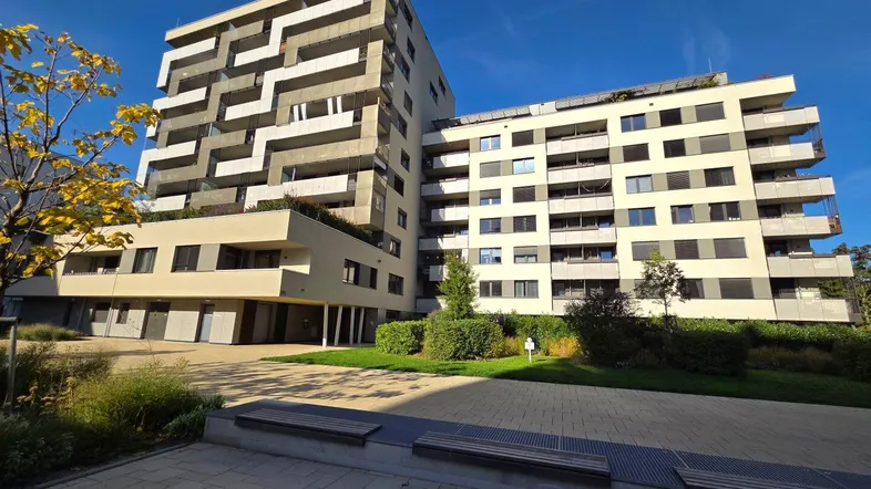 Modernes Apartmentgebäude mit mehreren Balkonen und gepflegten Grünflächen unter blauem Himmel.