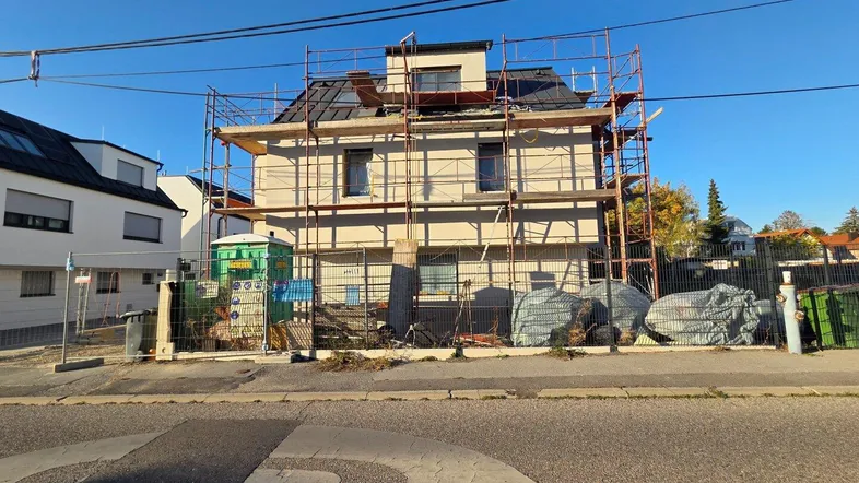 Neubau eines Mehrfamilienhauses mit Gerüst und Baustellenelementen in einer Wohngegend.