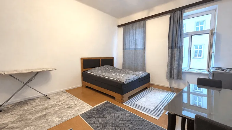 Helles Schlafzimmer mit Doppelbett, Esstisch und Parkettboden, dekoriert mit Teppichen.