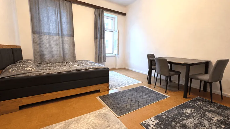 Helles Schlafzimmer mit Holzboden, einem Doppelbett und einem kleinen Essbereich am Fenster.