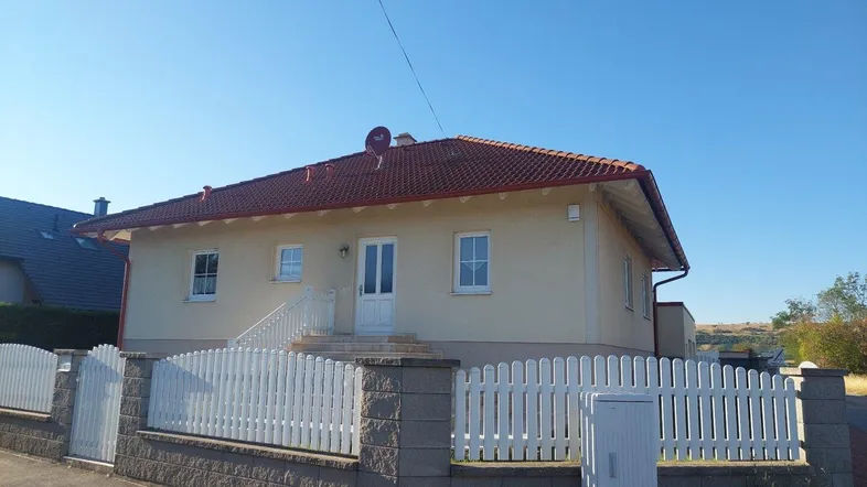 Vorderansicht eines Einfamilienhauses mit weißem Zaun und gepflegtem Vorgarten unter blauem Himmel.