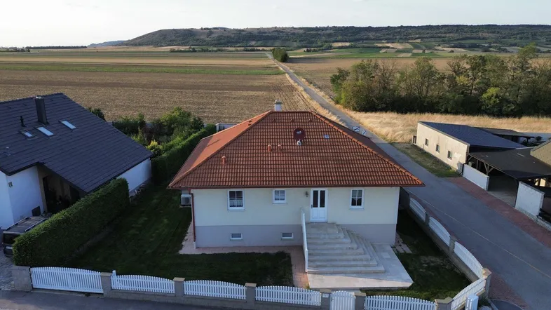 Luftaufnahme eines Einfamilienhauses mit rotem Ziegeldach, umgeben von Feldern und ländlicher Landschaft.