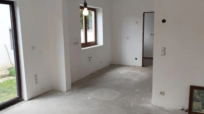Unfertiger Wohnbereich mit weißen Wänden, Betonboden und Fenster, bereit für den Ausbau.