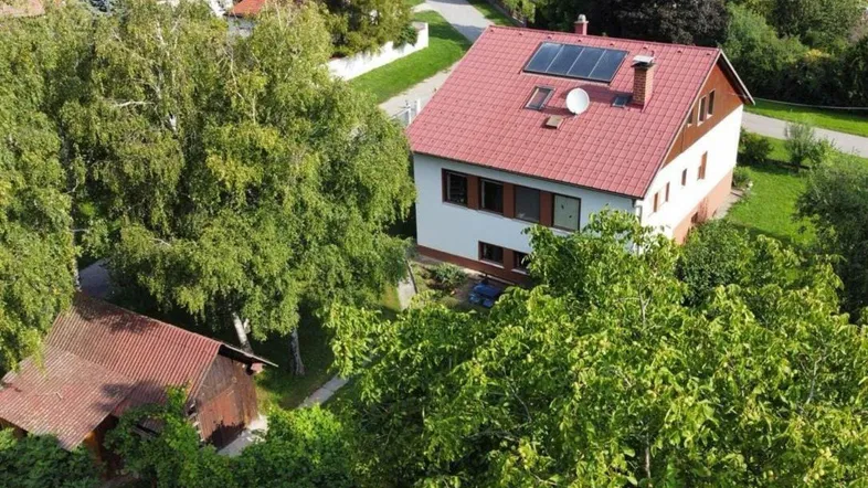 Luftaufnahme eines Einfamilienhauses mit rotem Dach, Solarpaneelen und viel Grün in ländlicher Umgebung.