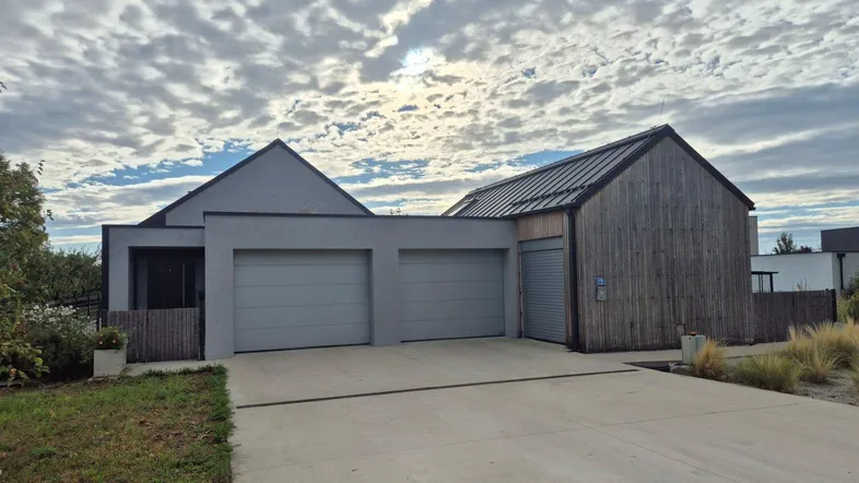 Modernes Einfamilienhaus mit Doppelgarage und Holzfassade unter bewölktem Himmel.