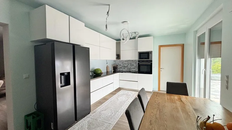 Moderne Küche mit weißen Schränken, schwarzem Kühlschrank und Essbereich mit Holztisch.