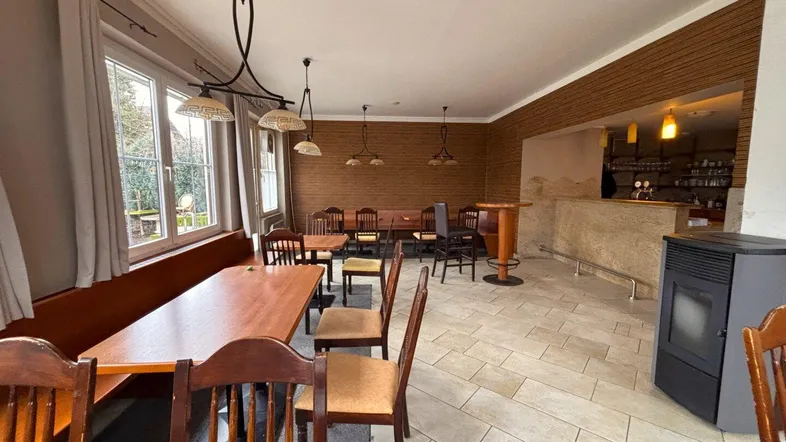 Geräumiger Gastraum mit Holztischen, Bänken und Fliesenboden, ideal für ein Restaurant oder Café.