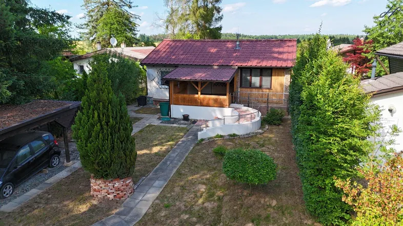 Luftaufnahme eines kleinen Hauses mit rotem Dach, überdachter Veranda und einem gepflegten Gartenbereich.