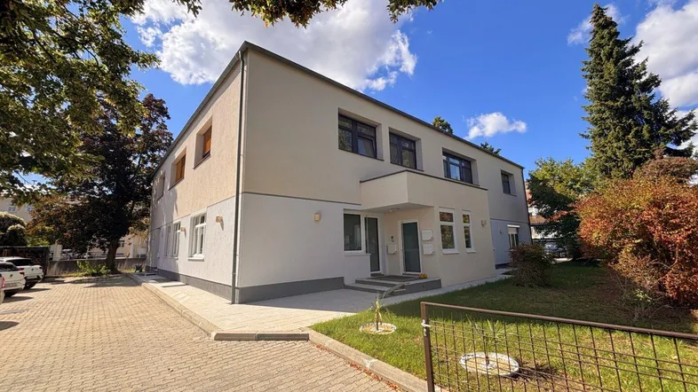 Modernes Mehrfamilienhaus mit heller Fassade und gepflegter Außenanlage unter blauem Himmel.