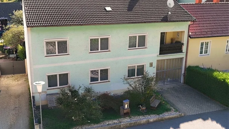 Hausfassade in Hellgrün mit Satteldach, Balkon und kleinem Vorgarten.