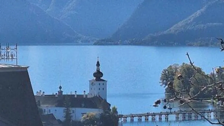 Malerischer Blick auf ein Schloss im See, umgeben von majestätischen Bergen unter blauem Himmel.