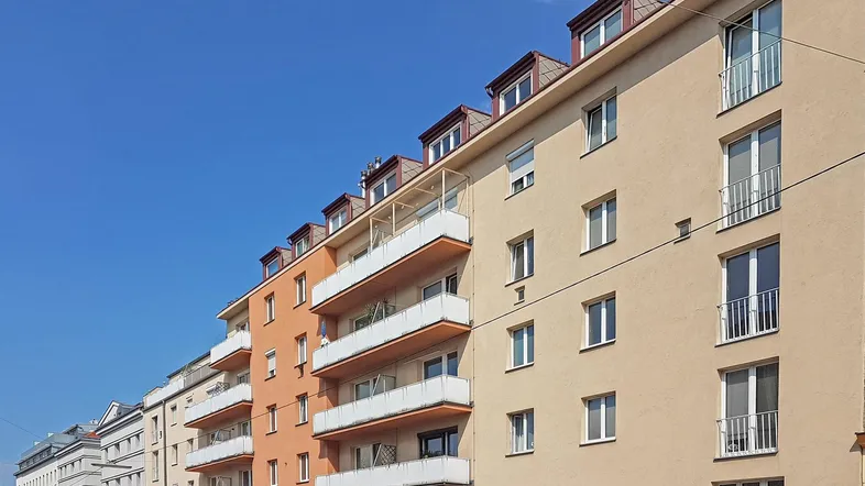 Mehrfamilienhaus mit mehreren Etagen und Balkonen unter blauem Himmel.