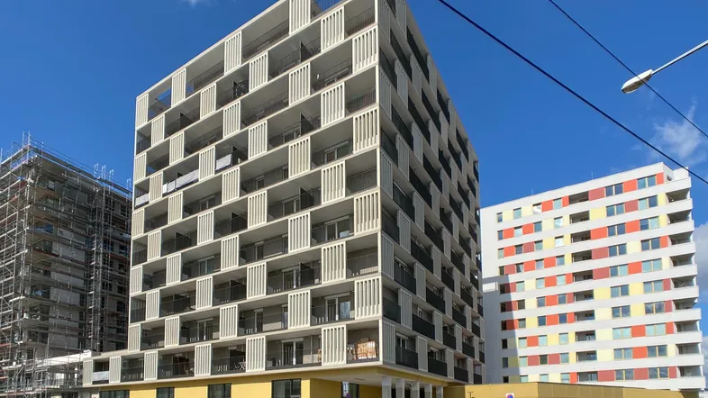 Modernes Wohngebäude mit markanter Fassade und Balkonen an einer städtischen Straße unter blauem Himmel.