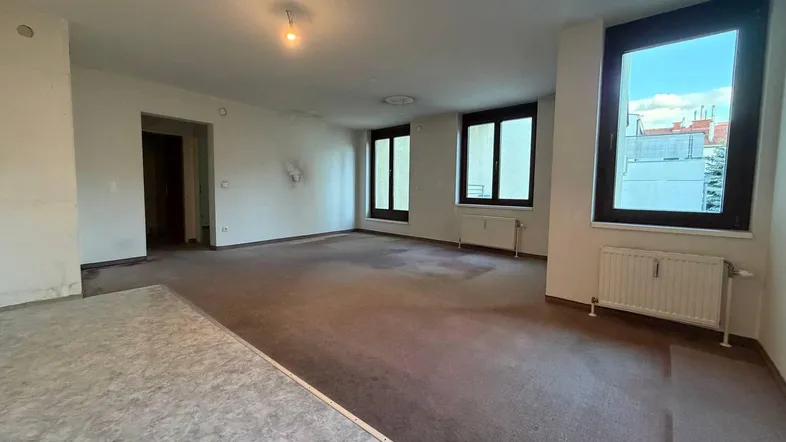 Geräumiger, unmöblierter Innenraum mit Teppichboden und Fenstern, bereit für Renovierung.