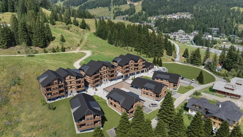 Luftaufnahme einer modernen Wohnanlage im Chalet-Stil, eingebettet in eine grüne Berglandschaft mit Wäldern.