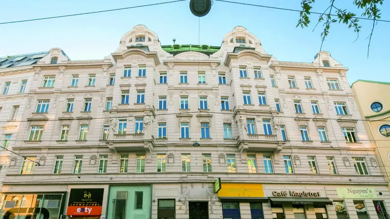 Klassisches Altbaugebäude mit vielen Fenstern und Geschäften im Erdgeschoss in einer Stadtansicht.