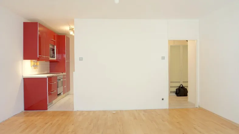 Heller offener Wohnbereich mit moderner roter Einbauküche und hellem Holzfußboden, ideal für modernes Wohnen.