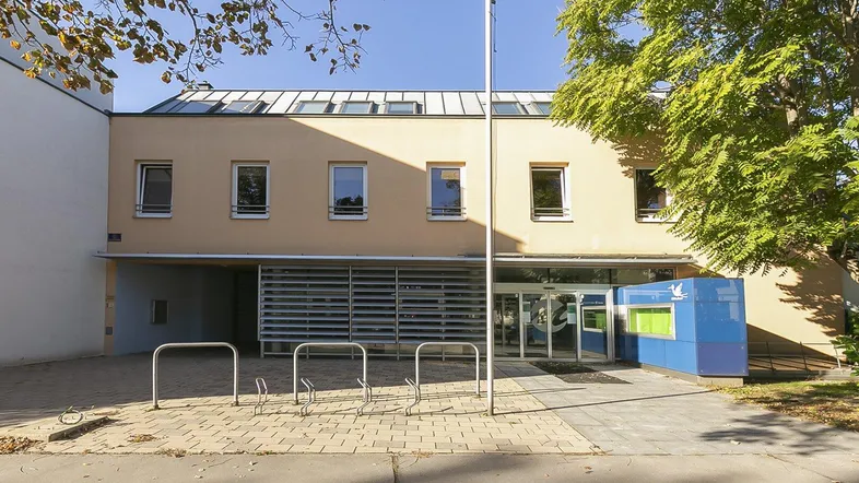Fassade eines modernen Gebäudes mit großen Fenstern, einem Eingangsbereich und Fahrradständern davor.
