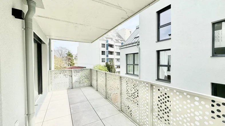 Geräumiger Balkon mit modernen Lochblechgeländern und Fliesenboden, umgeben von anderen Gebäuden.