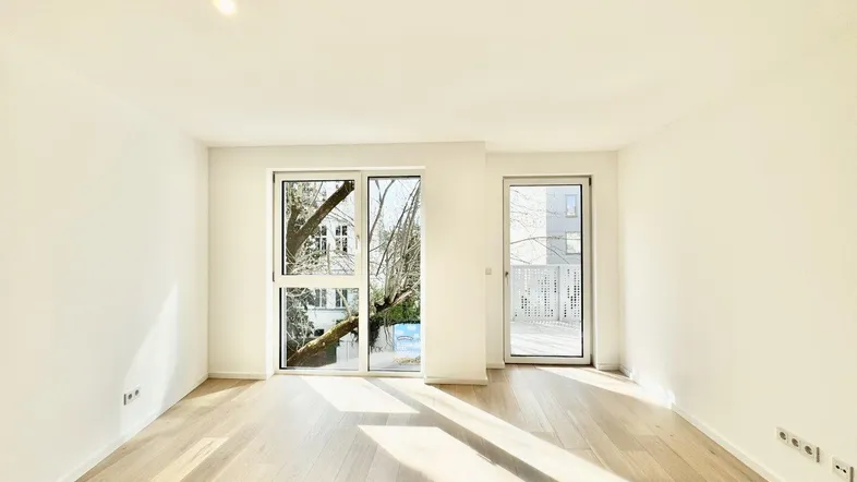 Helles Zimmer mit Holzboden und Zugang zu einem Balkon, ideal für Wohn- oder Schlafbereich.