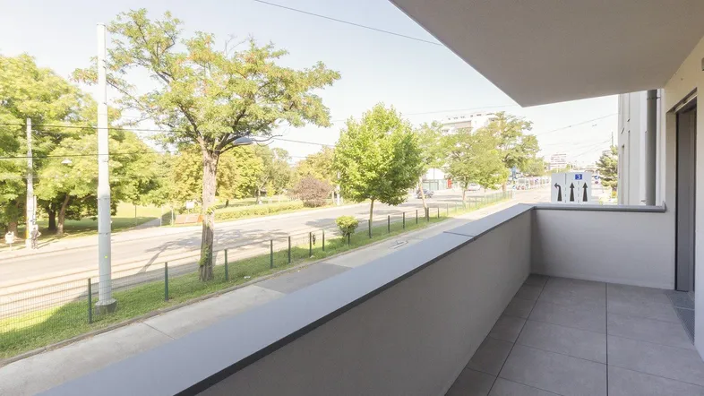 Geräumiger Balkon mit Fliesenboden und Blick auf die grüne Umgebung und die Straße.