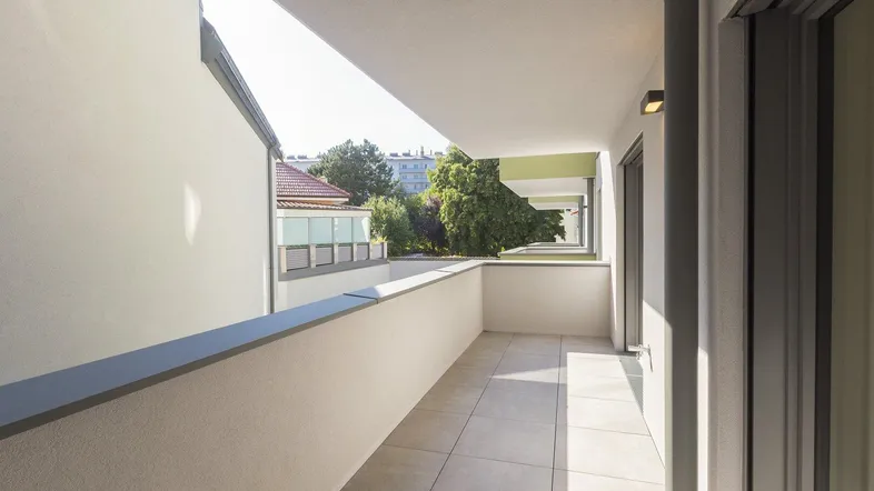 Langer, schmaler Balkon mit Fliesenboden und Blick auf die Umgebung.