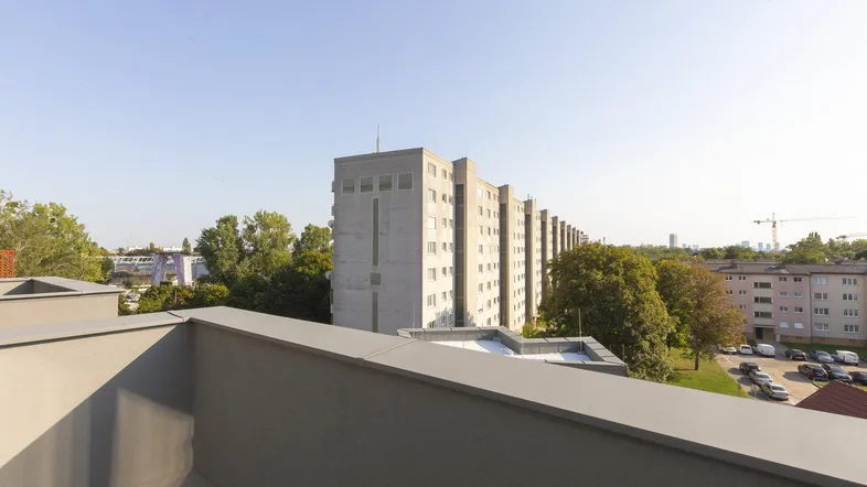 Blick von der Terrasse auf die umliegende Wohnbebauung und grüne Bäume unter klarem Himmel.