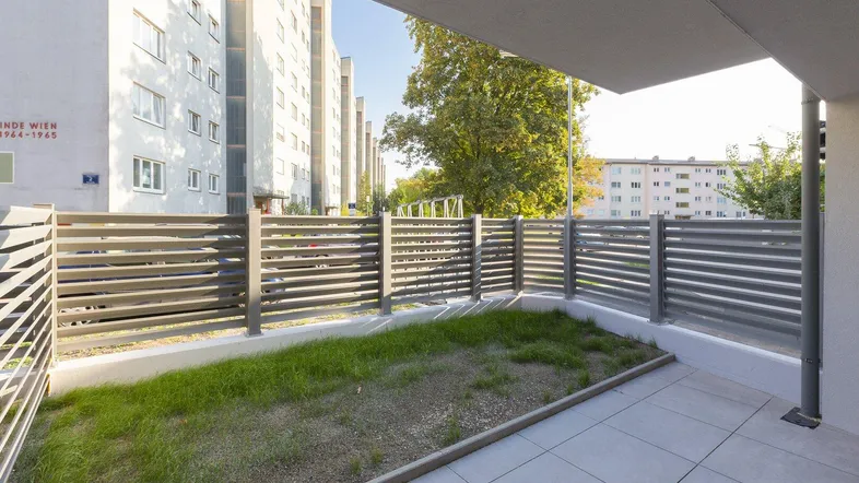 Kleine private Terrasse mit Fliesenboden und Grünfläche, umgeben von einem modernen Zaun.