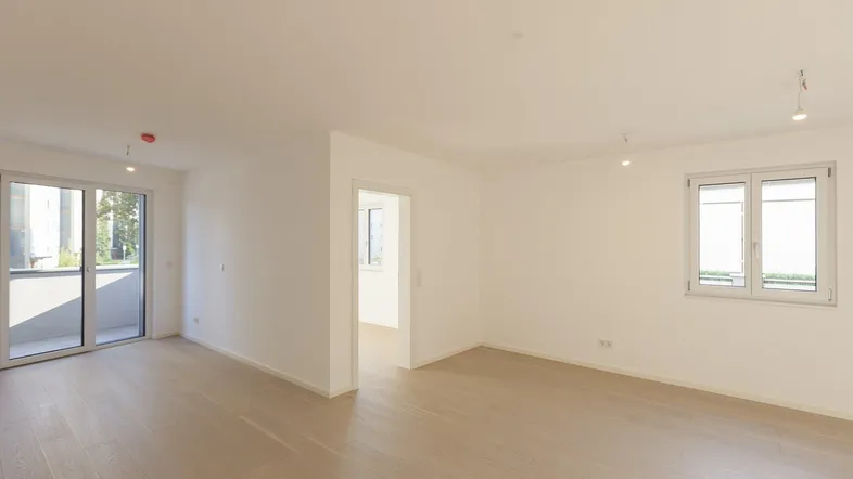 Helles, leeres Zimmer mit Holzboden und Zugang zu einem Balkon, ideal als Wohnbereich.