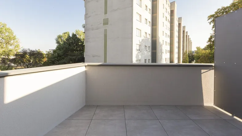 Heller Balkon mit Fliesenboden und Blick auf umliegende Gebäude und Grünflächen.