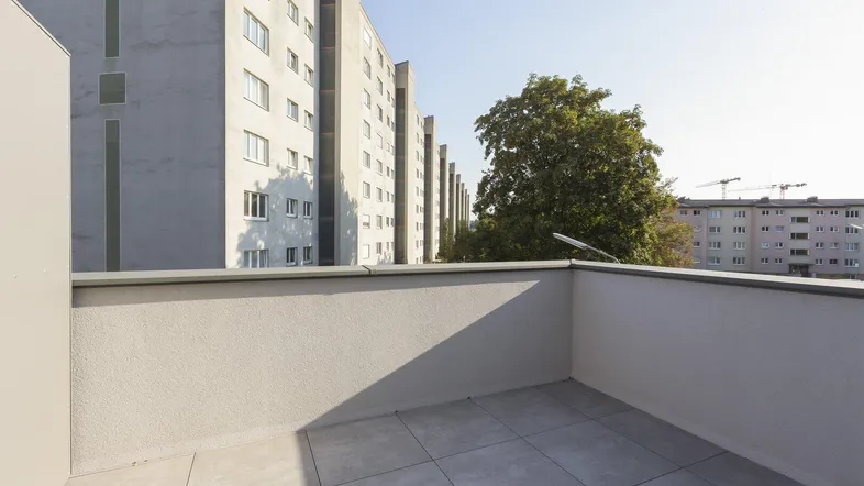 Geräumiger Balkon mit Fliesenboden und Blick auf umliegende Wohngebäude.