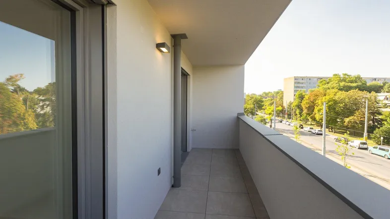 Geräumiger Balkon mit Fliesenboden und Blick auf die Straße sowie grüne Bäume.
