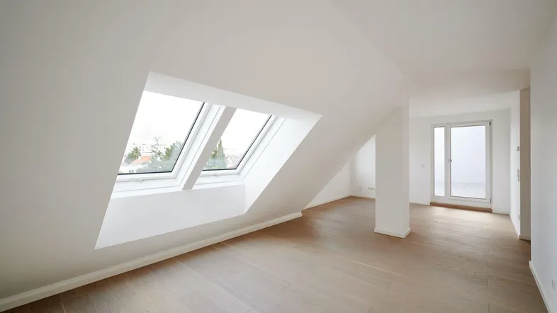 Heller Dachgeschossraum mit Holzboden und großen Dachfenstern, der viel Tageslicht hereinlässt.