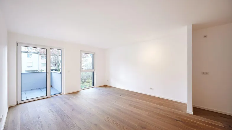 Helles, leeres Wohnzimmer mit modernem Holzparkettboden und Zugang zu einem Balkon.