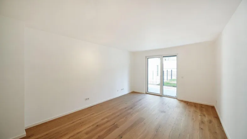 Heller, leerer Raum mit Holzboden und Zugang zu einem Außenbereich durch eine Glastür.