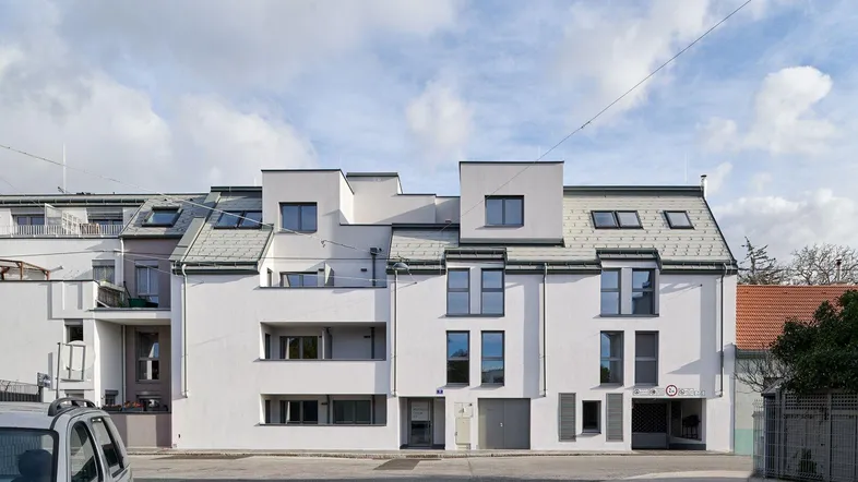 Moderne Wohnanlage mit weißer Fassade, Satteldach und integrierter Tiefgarage an der Straße.