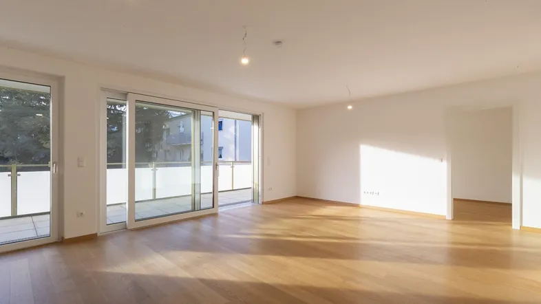 Heller Wohnbereich mit Holzboden und Zugang zu einem Balkon, durchflutet von natürlichem Sonnenlicht.