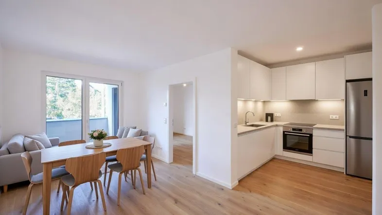 Heller offener Wohn-Essbereich mit integrierter Küche, Parkettboden und Zugang zum Balkon.