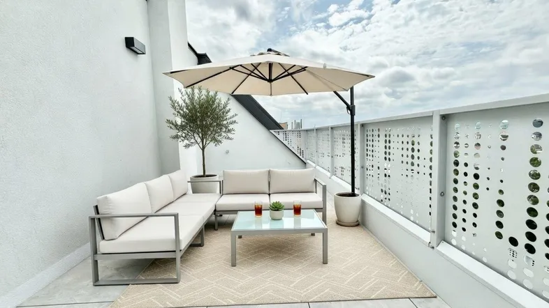 Moderne Dachterrasse mit bequemen Loungemöbeln, Sonnenschirm und Blick auf die Umgebung.