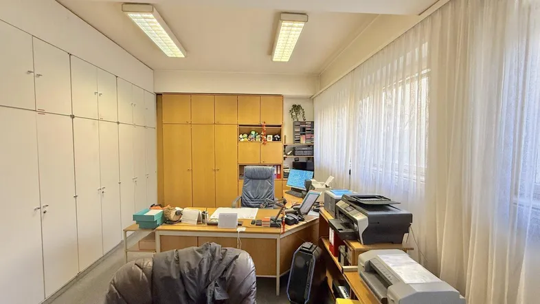Geräumiges Büro mit großem Schreibtisch, vielen Aktenschränken und natürlichem Lichteinfall durch die Fenster.