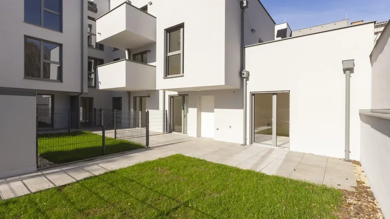 Gepflegter Gartenbereich mit Rasenfläche und angrenzender Terrasse vor einem modernen Wohngebäude.