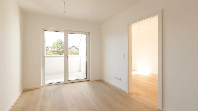Helles Zimmer mit Holzboden und Zugang zu einem kleinen Balkon, bereit zur individuellen Gestaltung.