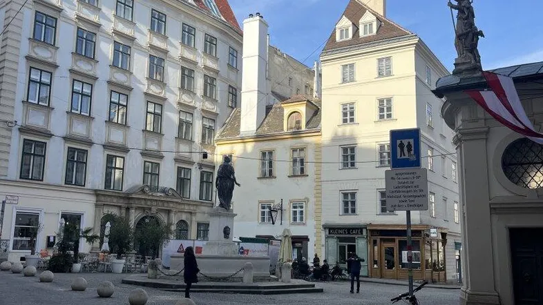 Historischer Platz in Wien mit traditionellen Gebäuden und einem Denkmal unter blauem Himmel.